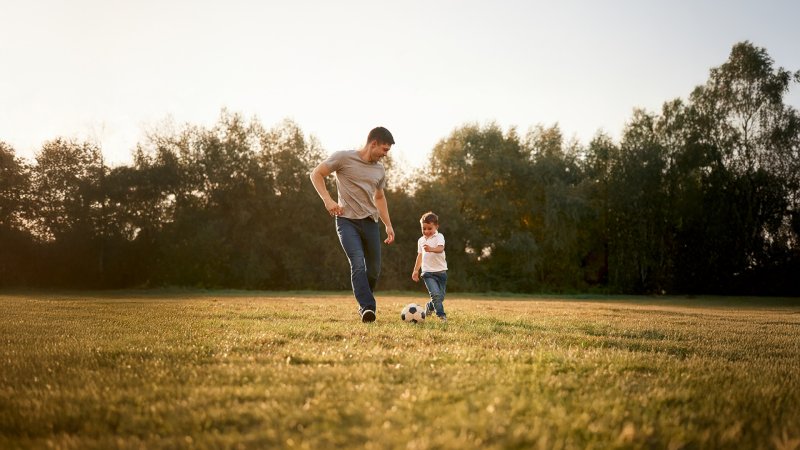 A father and son playing soccer outdoors.