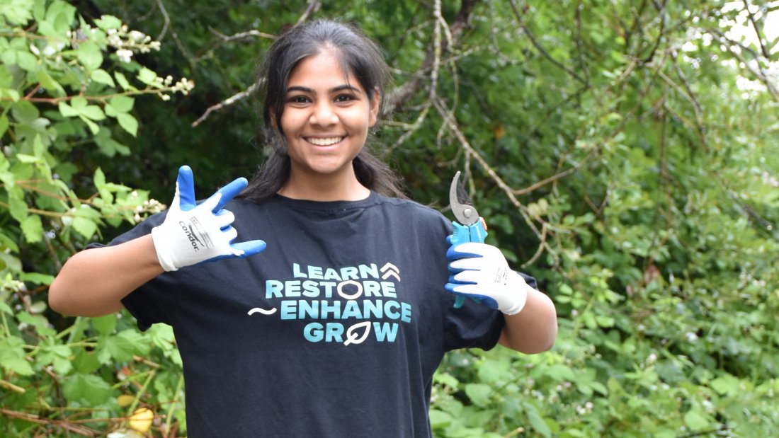 youth volunteer smiling in a forest with "Learn Restore Enhance Grow" tshirt