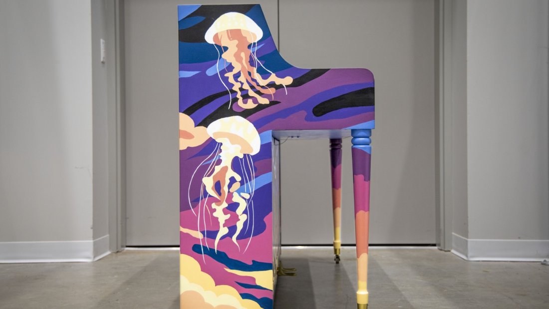  A painted piano with an underwater ocean theme, featuring coral and fish, on display in an indoor setting.