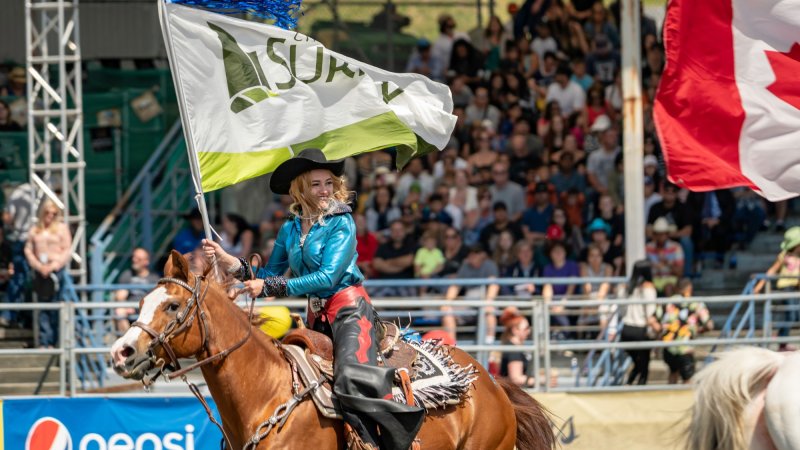 a woman rides a horse in an arena with a city of surrey flag