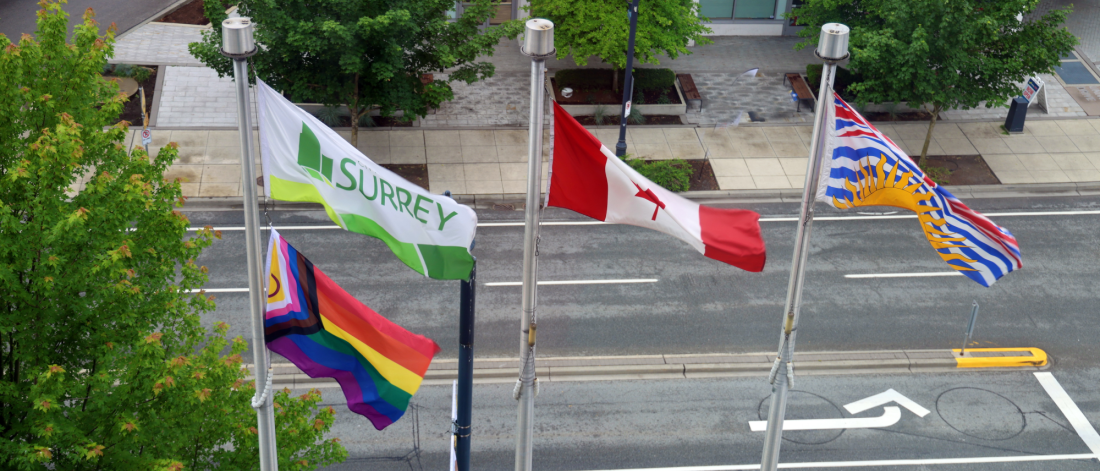 Pride flag, City of Surrey flag, Canada flag, and British Columbia flag