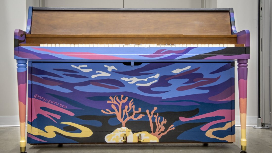 A painted piano with an underwater ocean theme, featuring coral and fish, on display in an indoor setting.