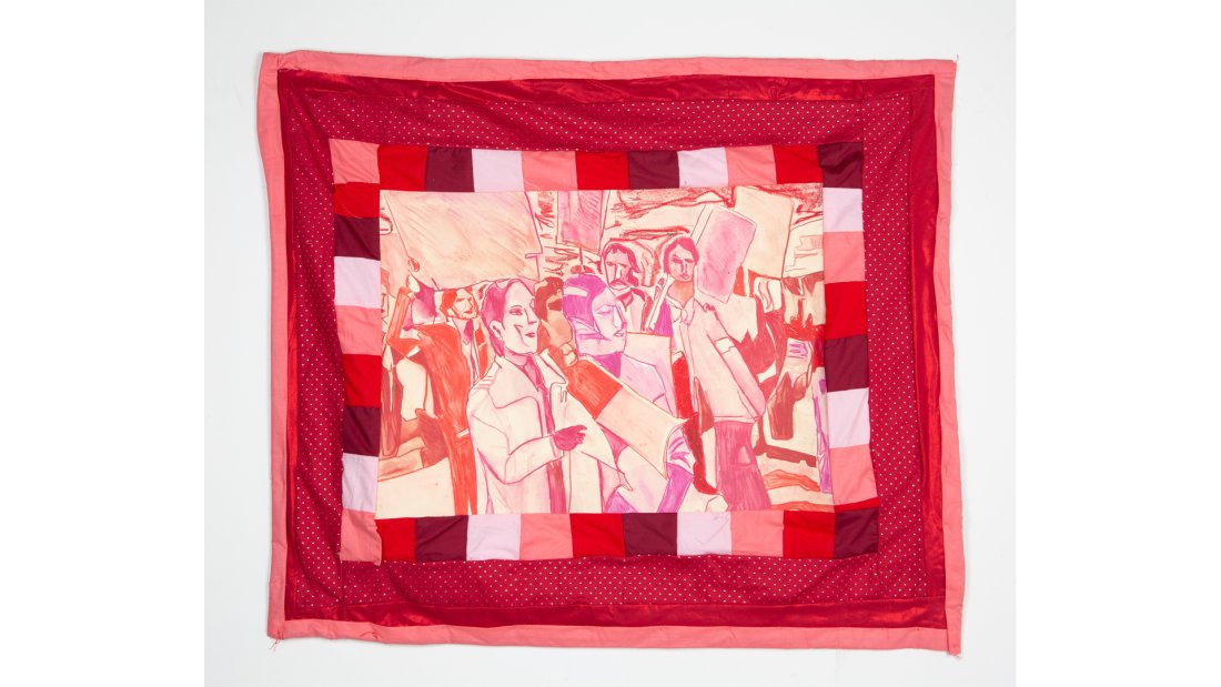 Quilt of various reds bordering a scene of a protest with farmworkers holding up signs and speaking into megaphones.