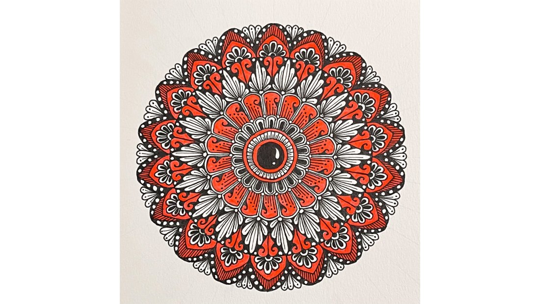 A mandala in the shape of a flower made with red and black ink.