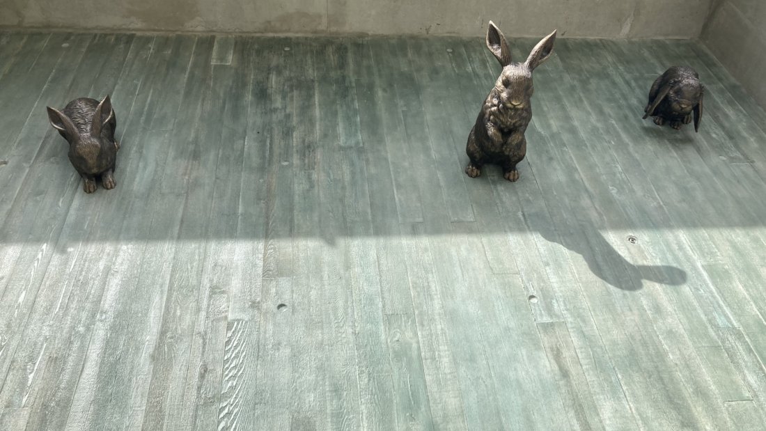 Three bronze rabbit sculptures placed on a textured concrete floor.