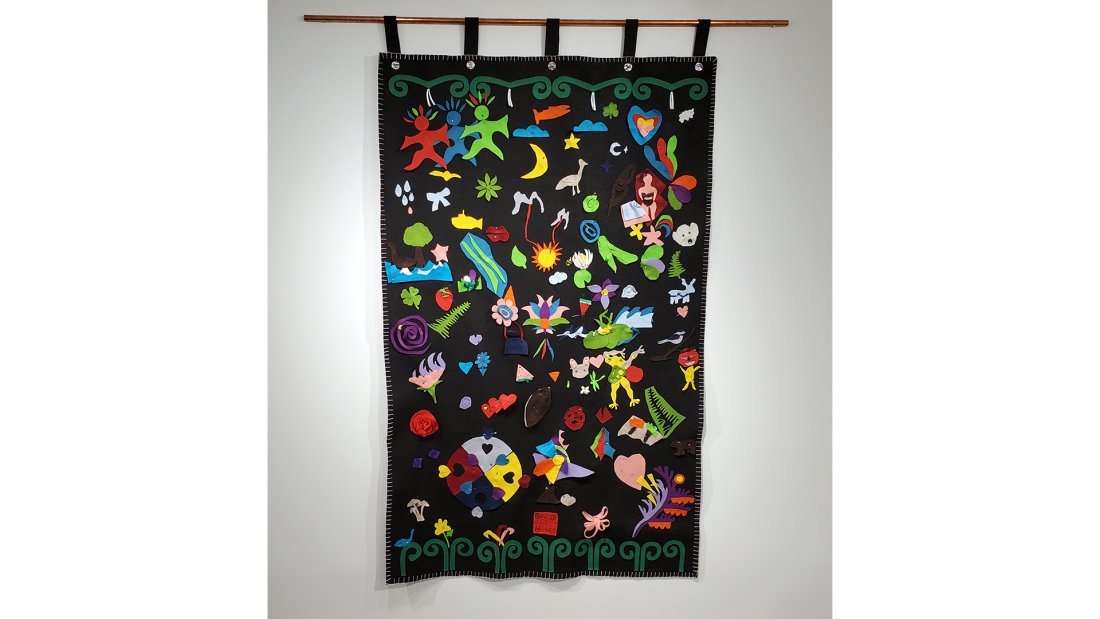 A black felt blanket with multi-coloured felt pieces hangs on the wall.