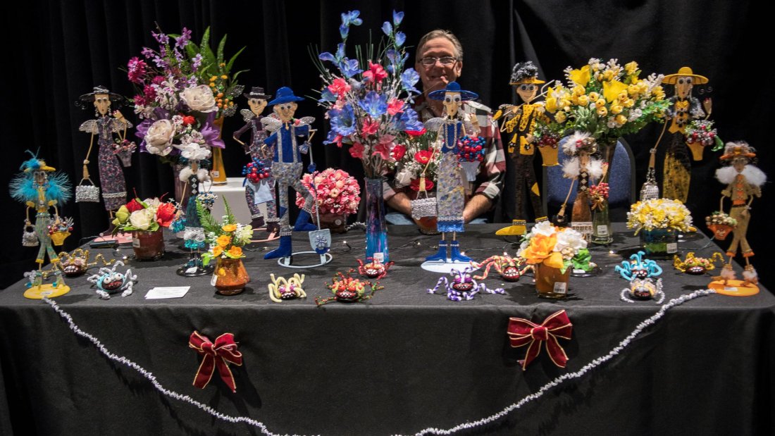 A table full of colourful flowers and miniature metal sculptures of women carrying purses and other accessories.