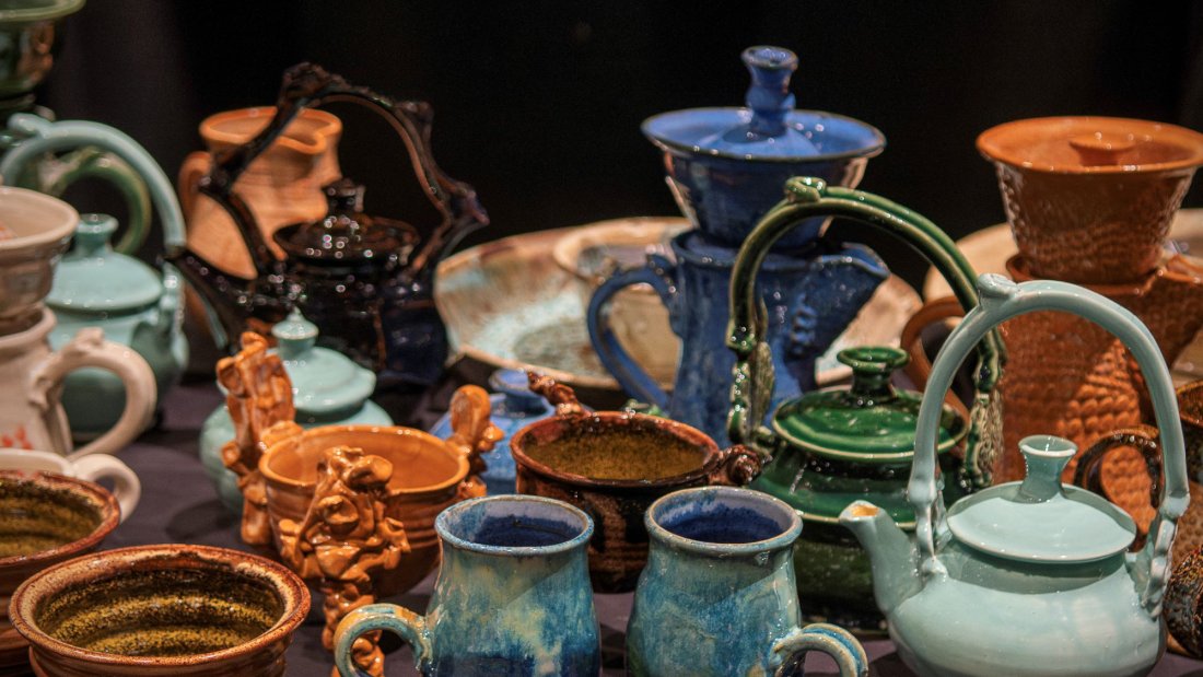 A table full of a variety of functional pottery including mugs, teapots, and bowls.