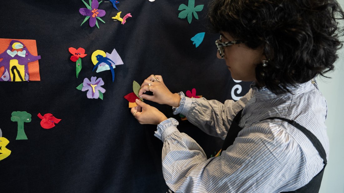 A woman attaching felt cutouts of leaves to a blanket hanging on the wall.