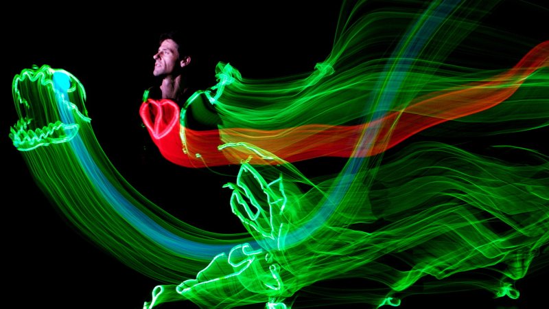 performer against a black background with swirling lights of green, blue and red in the shape of a dinosaur