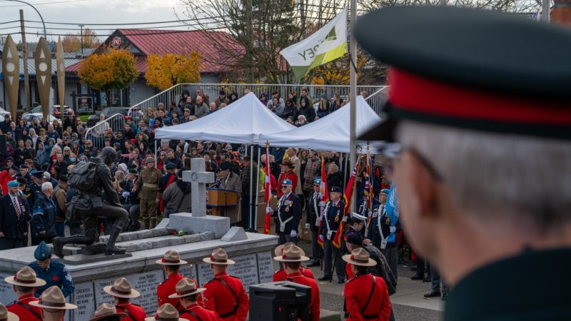 A Remembrance Day ceremony with uniformed individuals in red jackets and attendees around a soldier statue paying respect.