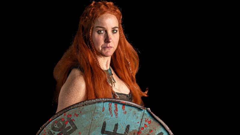 The Shield Maiden stares into the camera holding her Viking shield.