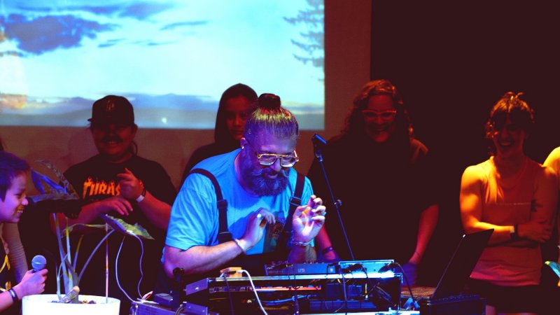 Ruby Singh (aka Ruploops) on performing on stage, projection in the background, audience of all ages around him, young person holding a microphone