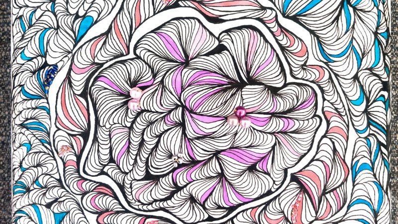 An intricate patterned drawing resembling a flower with blue, pink, purple, and black ink used