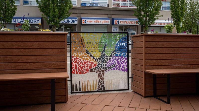 Colorful mosaic artwork on a gate in an urban outdoor seating area.