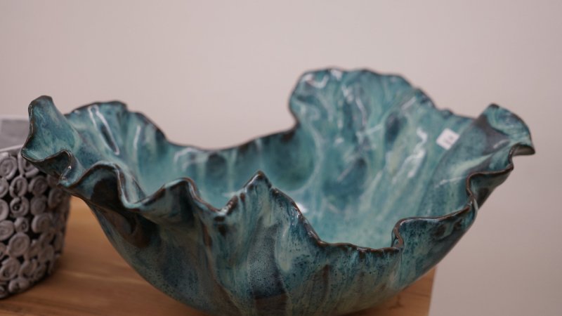 Close-up of a handmade ceramic bowl with a wavy rim, glazed in shades of turquoise and blue.