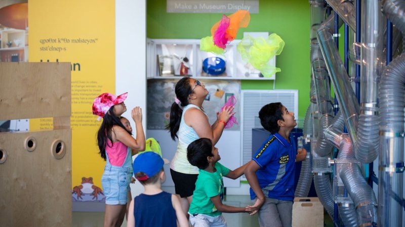 Children engage with interactive exhibits at a museum, playing with colorful floating materials and observing tubing systems