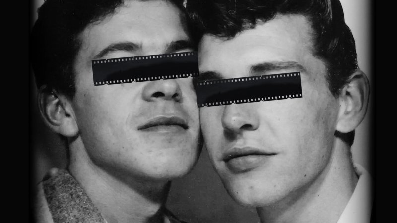 Black and white photograph of two men, their eyes covered over by celluloid tape