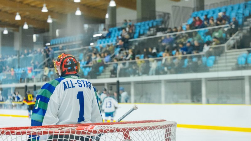 Hockey goalie wearing an 'All-Star' jersey stands in front of the net during a game, with spectators in the background.