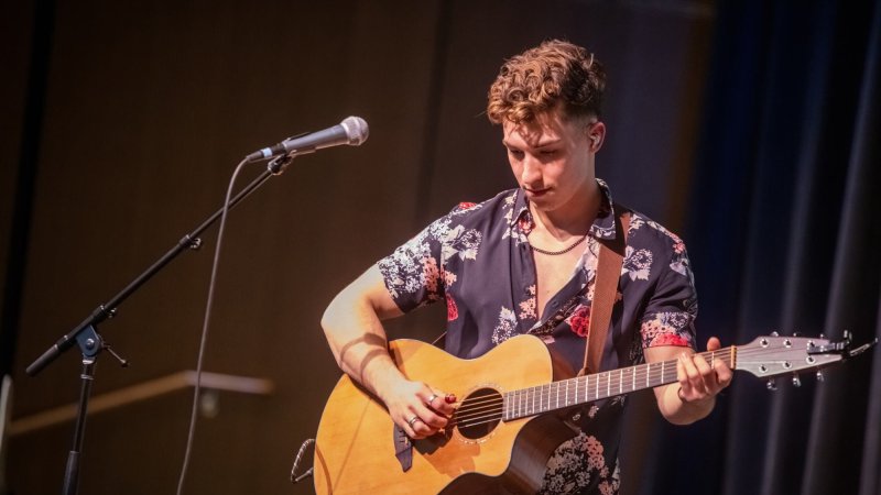 Musician performing on stage with an acoustic guitar.