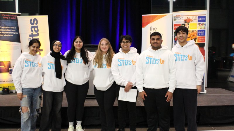 Group of seven youth standing in front of a stage wearing Surrey Steps Up hoodies. 