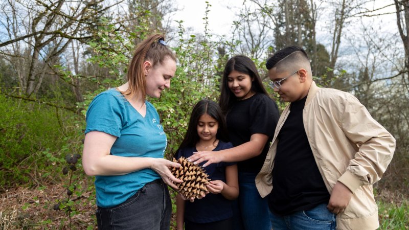 three children look at a large pinecone that an instructor is showing them