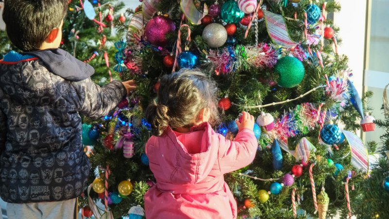 Two young children decorating a Christmas tree with colorful ornaments and tinsel.