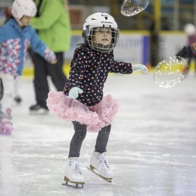 A child skating in a pink tutu with bubbles in the air.