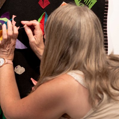 A crouching woman attaches a piece of felt to a blanket hanging on the wall.