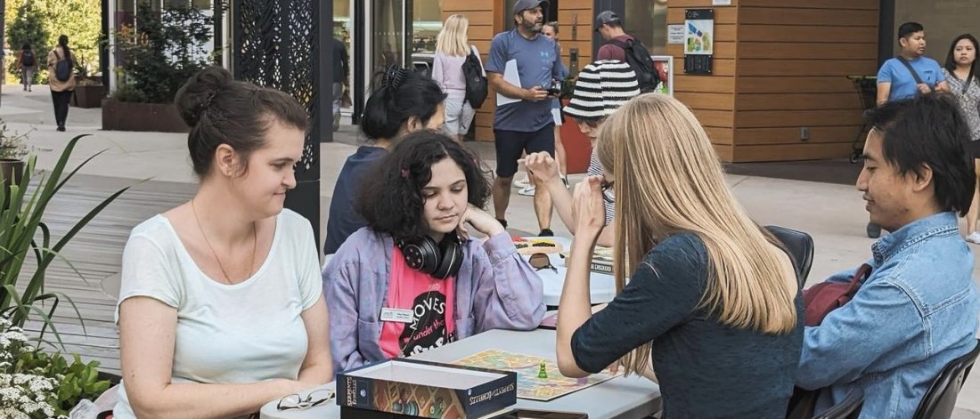 People enjoying a board game at an outdoor table in a lively urban setting.