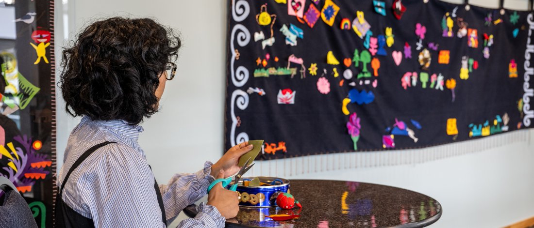 A woman sits next to a felt blanket hanging on the wall.