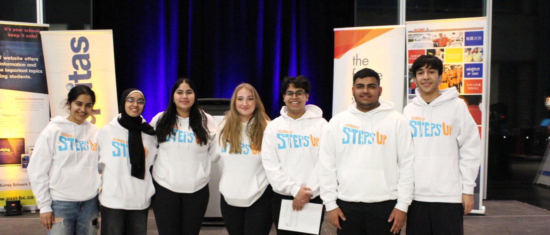 Group of seven youth standing in front of a stage wearing Surrey Steps Up hoodies. 