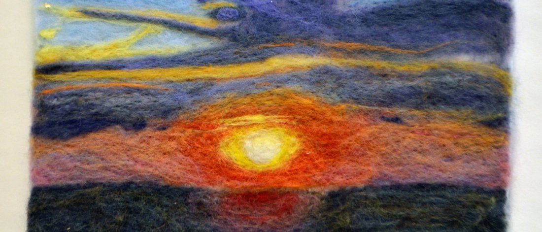 a felted picture of a pink-orange-yellow sunset over dark water with a blue and yellow sky above