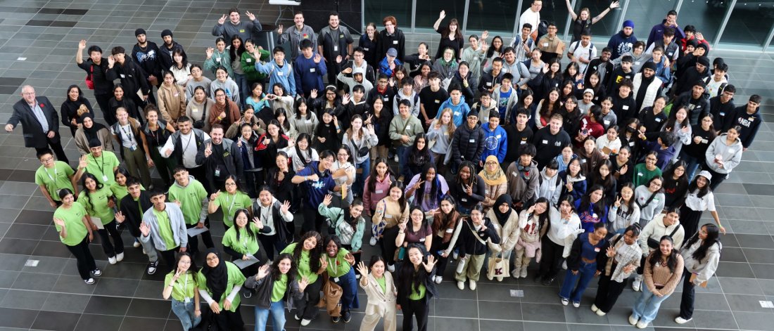 Large group of diverse young people smiling and waving at a community event.