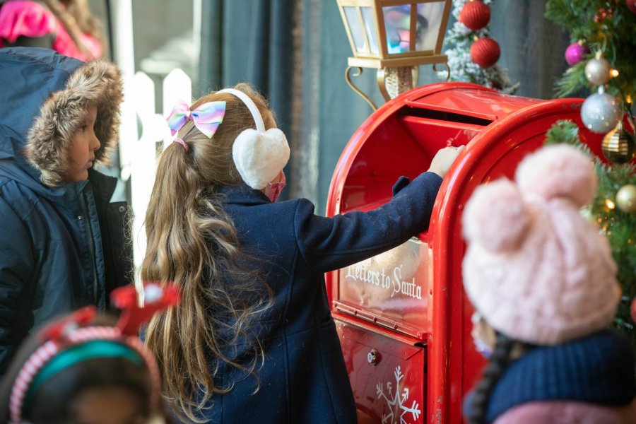 Children mailing letters to Santa at a festive red mailbox decorated for Christmas.