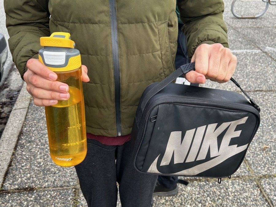 A person holding a black lunch bag and a yellow water bottle.