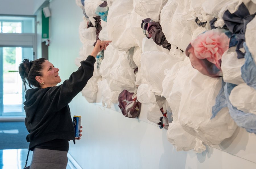 A woman is adjusting an intricate wall installation made of variously colored fabric scraps.