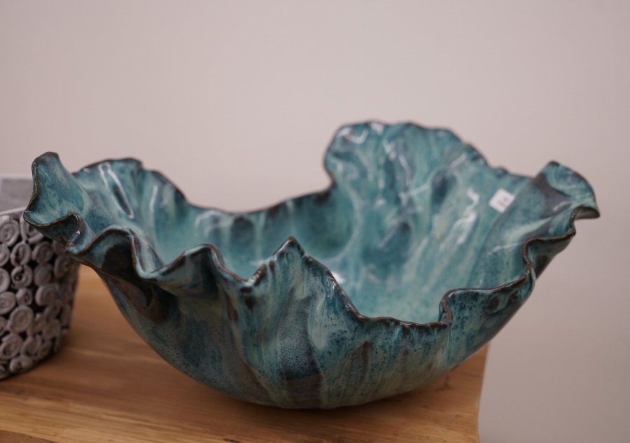 Close-up of a handmade ceramic bowl with a wavy rim, glazed in shades of turquoise and blue.