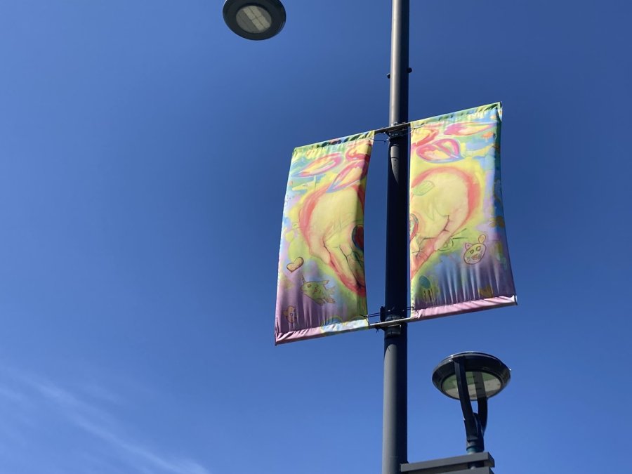 Colorful banners featuring abstract designs mounted on a lamp post against a clear blue sky.