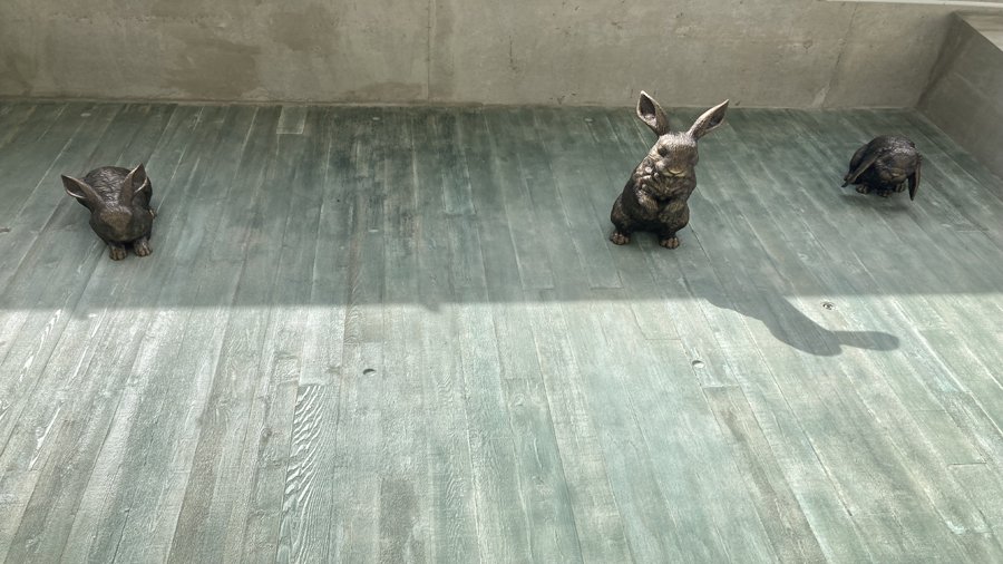 Three bronze rabbits look down at viewers from a concrete wall.