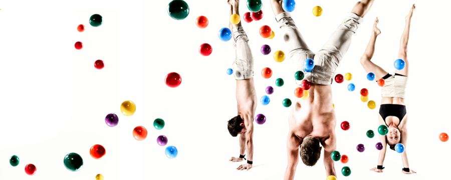 three acrobats doing handstands against a white background with 50 or more coloured balls bouncing all around them